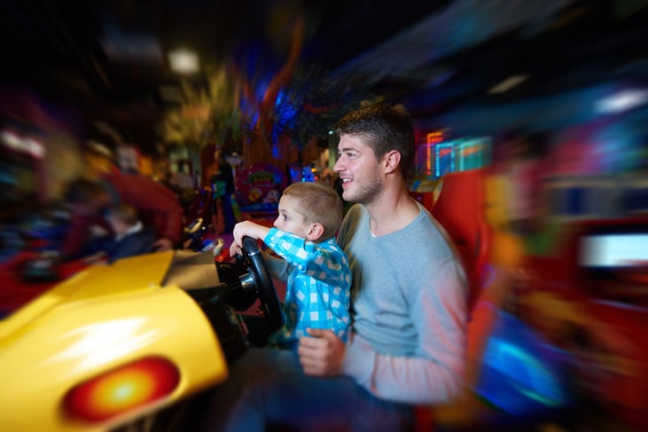 happy father and son playing driving wheel video game in playground theme park